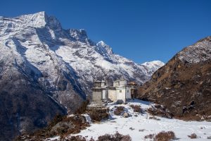 Tibetanisch wirkende Gebäude im Tal zwischen teilweise mit Schnee bedeckten Bergen