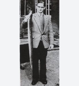 Ein Mann in einem feinen Anzug hält einen großen, toten Aal hoch