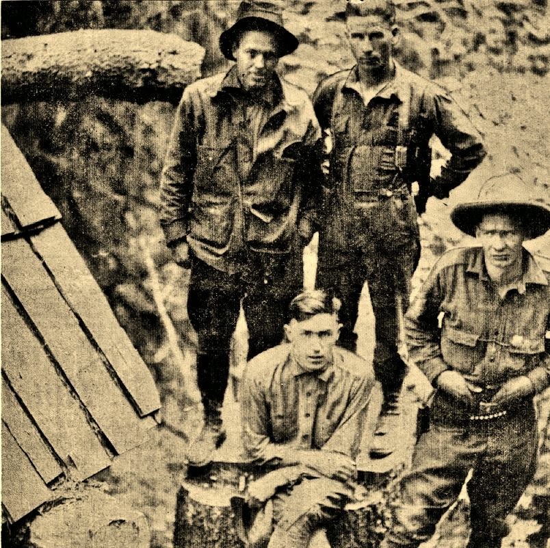 Vergilbte Fotoaufnahme von vier Männern, die an einer Bretterhütte stehen